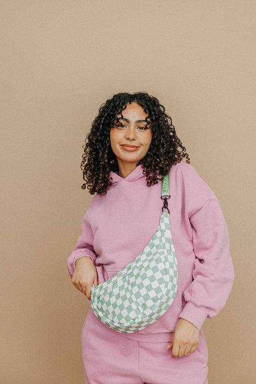 Person wearing a pink outfit with a green checkered bag against a beige background