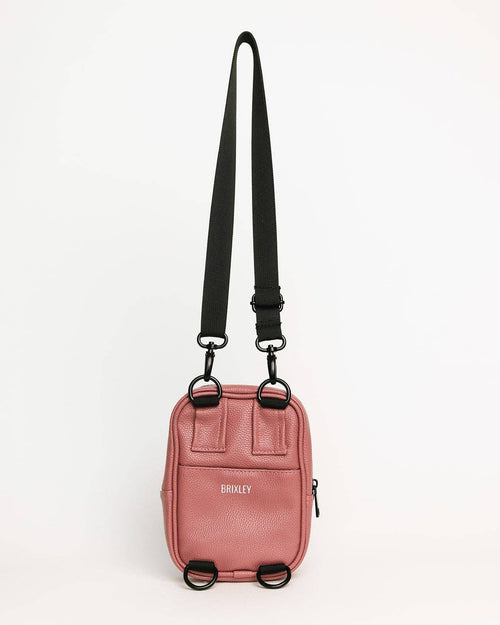 A pink textured leather crossbody bag with a black adjustable shoulder strap and black hardware, featuring the brand name 'BROOKLY' on the front, set against a plain white background.