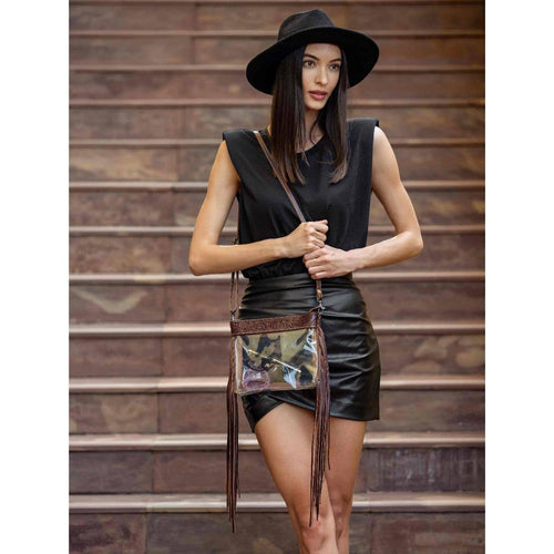 Woman in black outfit with a clear handbag featuring brown fringe, standing on wooden steps.
