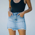 Person wearing a black tank top and light blue denim skirt with a white background