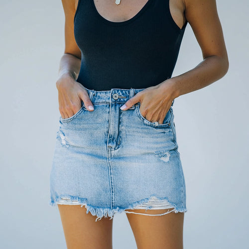 Person wearing a black tank top and light blue denim skirt with a white background