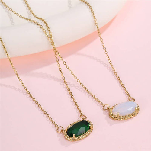 Two gold necklaces with green and white stones on a pink background