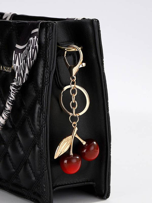 Black quilted handbag with a gold keychain featuring red cherries on a light gray background
