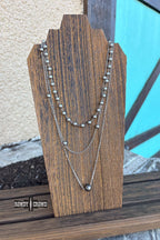 Three silver necklaces on a wooden stand with a blurred background