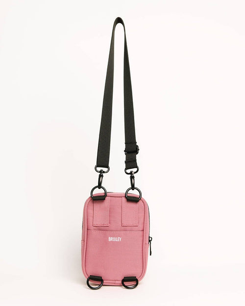 Pink crossbody bag with a black strap on a white background