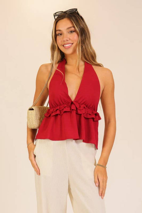 Woman wearing a red halter top with ruffles and white pants against a beige background
