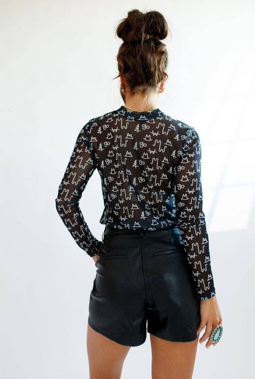 Person wearing a patterned long-sleeve shirt and black shorts on a white background