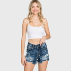 Woman wearing a white crop top and denim shorts on a plain background