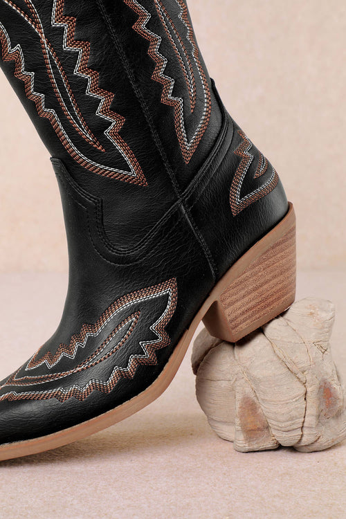 Black cowboy boot with brown stitching on a beige background