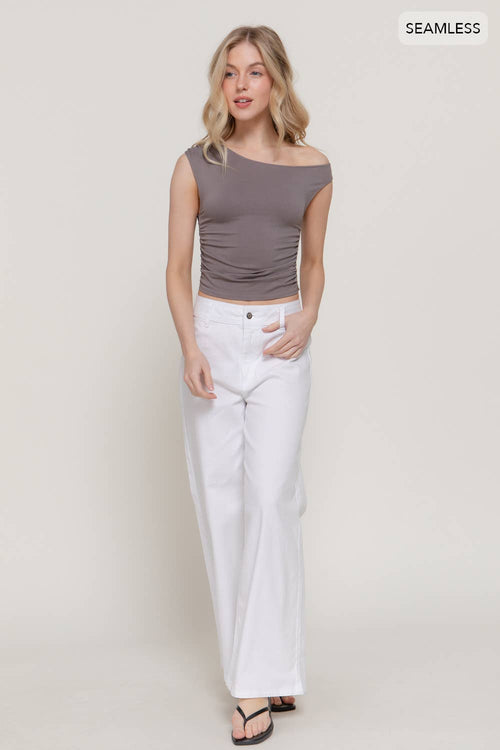 Woman wearing a brown off-shoulder top and white pants on a plain background