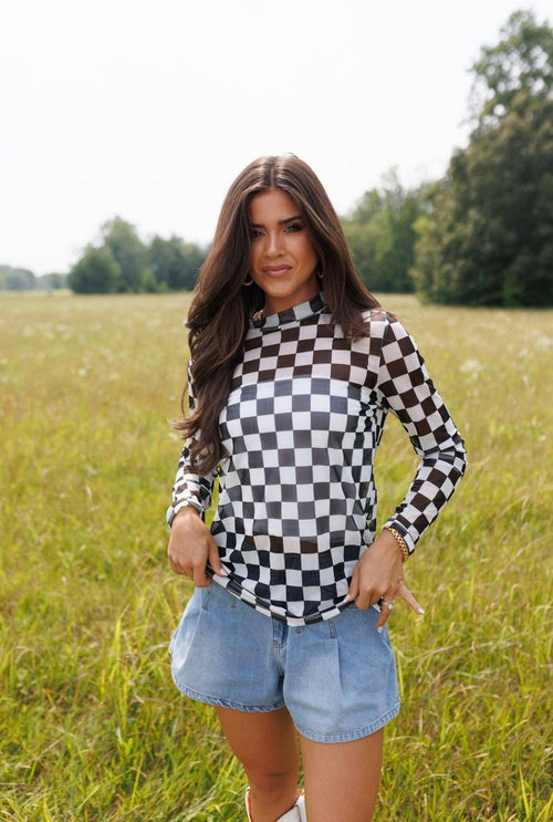Woman wearing a checkered shirt and denim shorts standing in a grassy field.