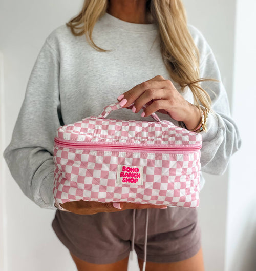 Person holding a pink checkered bag with a visible brand logo against a neutral background