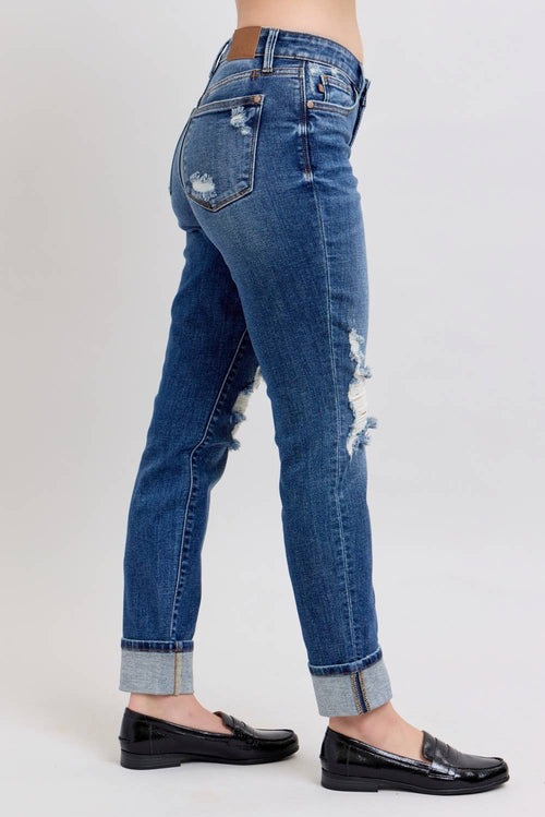 Blue jeans with distressing details worn by a person on a white background