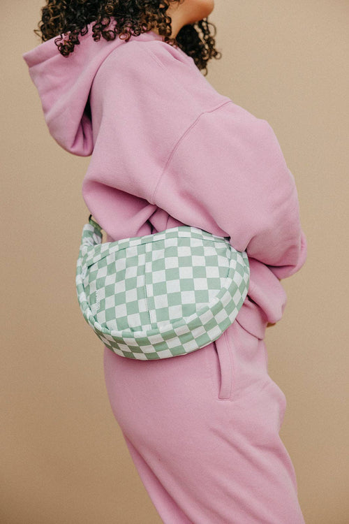 Person wearing a pink hoodie and pants with a green checkered bag on a beige background