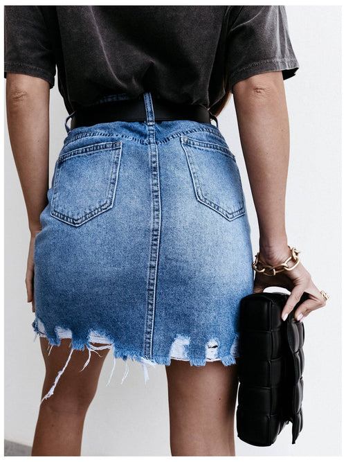 Person wearing a blue denim skirt with a plain background