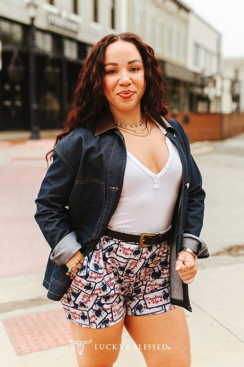 Woman wearing a denim jacket, white top, and patterned shorts on a city street.