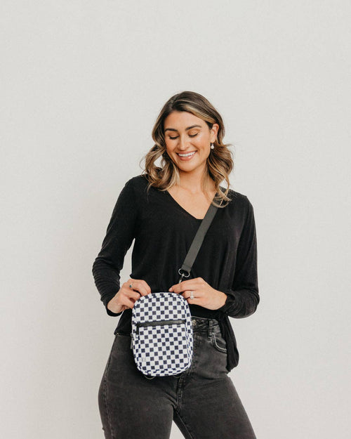 Woman wearing a black crossbody bag with a checkered pattern on a plain background