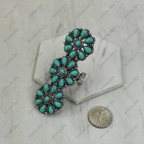 Turquoise and silver brooch on a gray background with a coin for scale.