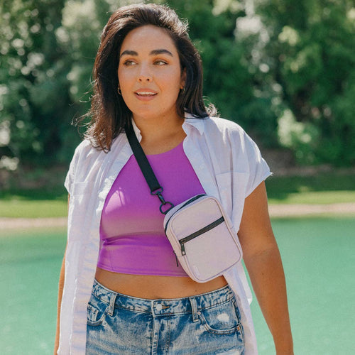 Woman wearing a purple top and denim shorts with a beige crossbody bag outdoors.