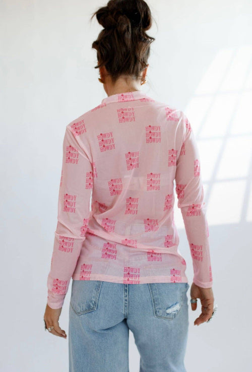Person wearing a pink long-sleeve shirt with red text and light blue jeans on a white background