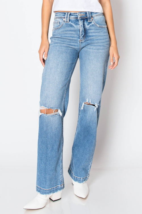 Light blue high-waisted straight-leg jeans with distressed rips at the knees, shown on a model wearing white pointed-toe boots against a white studio background.