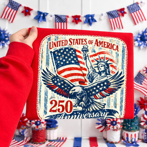 Card with 'United States of America 250th Anniversary' design held by a person in a red sleeve, with American flags and decorations in the background.