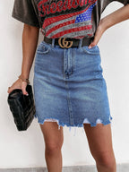 Person wearing a denim skirt with a black belt and holding a black clutch against a white background