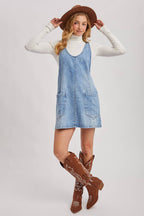 Woman wearing a denim dress, white turtleneck, and brown cowboy boots on a light gray background