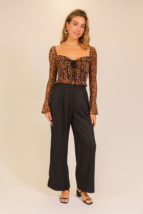 Woman wearing a leopard print top and black pants on a beige background