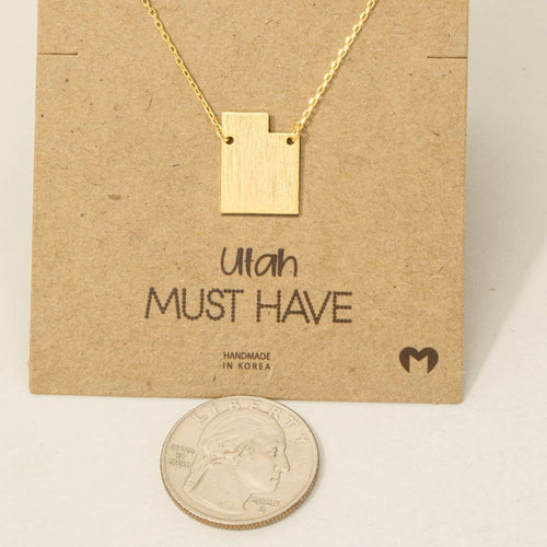 Gold necklace shaped like the state of Utah on a brown card with 'Utah MUST HAVE' text.