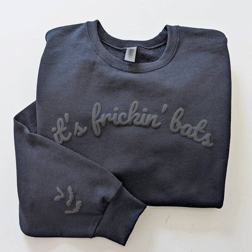 A dark charcoal gray sweatshirt with 'it's frickin' bats' embroidered in matching gray across the chest, folded neatly on a white background.