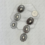 Silver concho-style earrings on a textured white surface with a coin for scale.