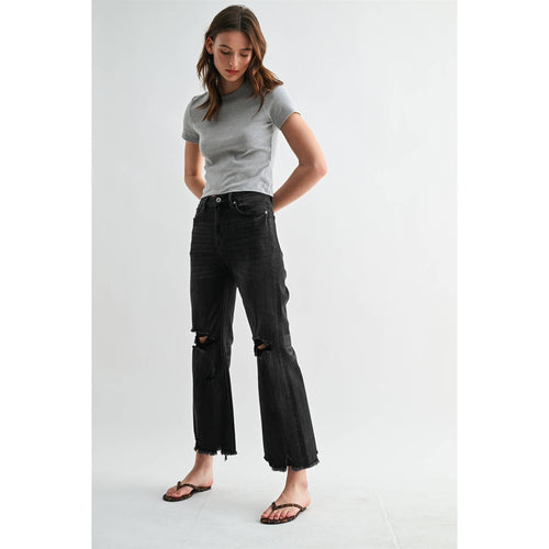 Woman wearing a gray t-shirt and black ripped jeans on a white background