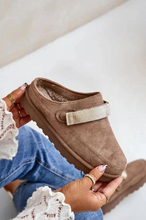 Brown slip-on shoes with a strap held by a person wearing blue jeans.