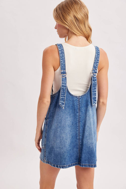 Woman wearing a denim pinafore dress on a light gray background