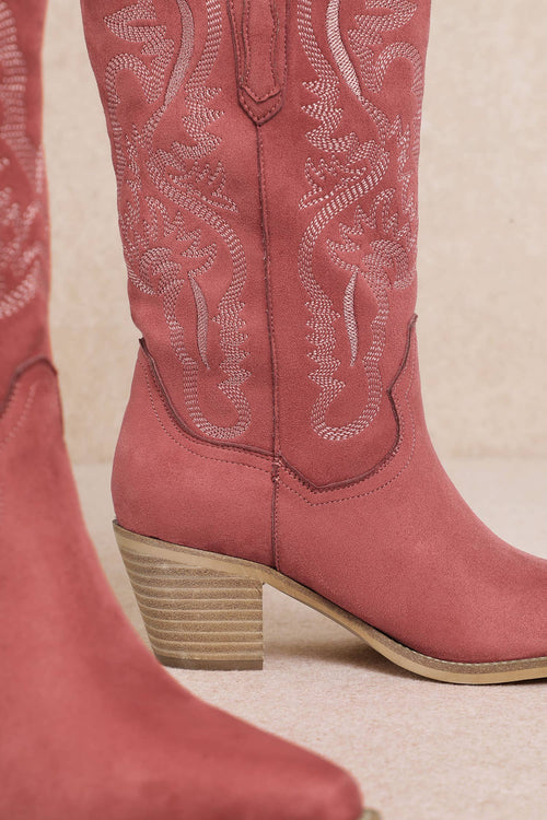 Close-up of pink cowboy boots with detailed stitching on a beige background