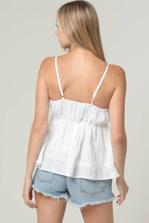 Woman wearing a white lace top and denim shorts on a plain background
