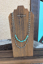 Necklace with turquoise stones on a wooden stand with 'Randy Crowe' branding.