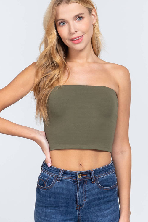 Woman wearing an olive green strapless top and blue jeans on a light gray background