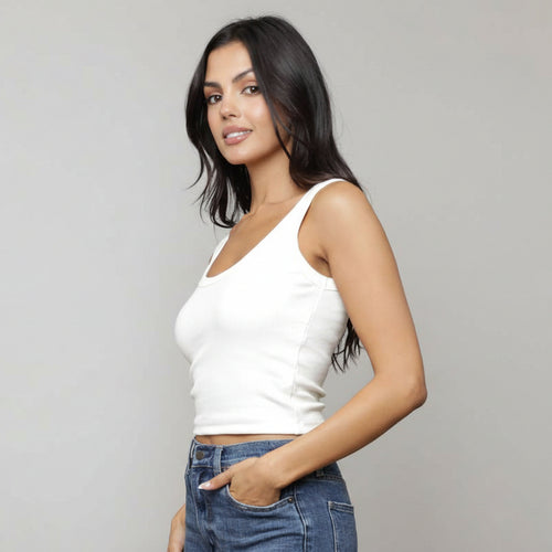 Woman wearing a white tank top and blue jeans with a neutral background