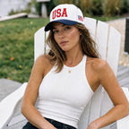 Woman wearing a 'USA' cap sitting on a white chair outdoors.