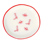 Round white plate with red rim featuring pink cowboy boot and hat designs on a white background