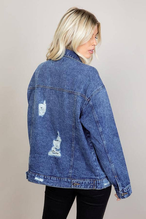 Person wearing a blue denim jacket with patches on a plain background