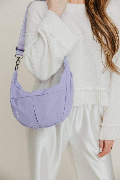 Person holding a purple shoulder bag against a neutral background