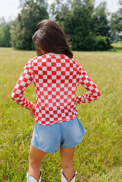 Person wearing a red and white checkered shirt and denim shorts standing in a grassy field.