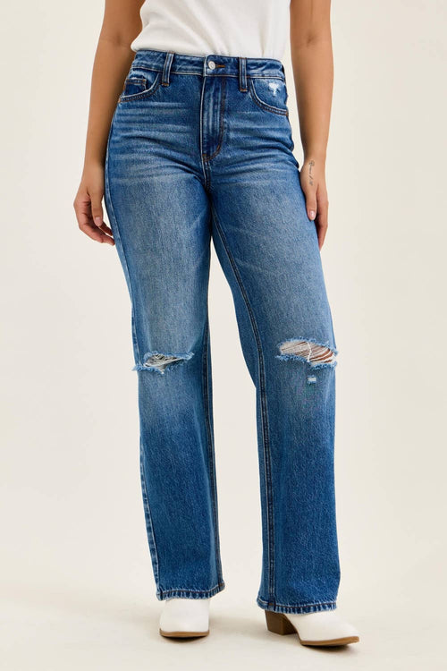 Person wearing blue jeans with slight distressing on a plain background
