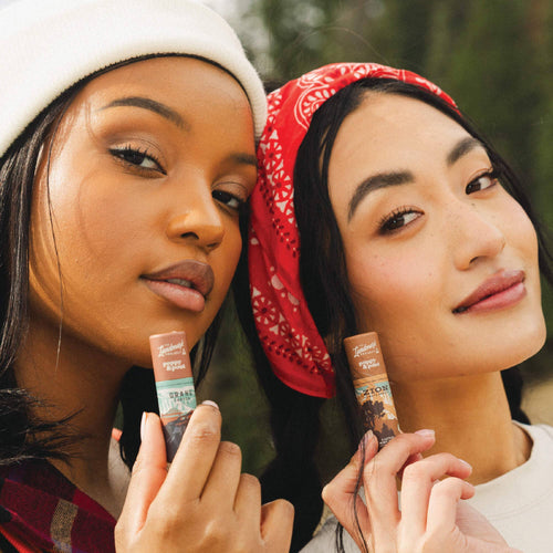 Two women holding and showing lip balms outdoors