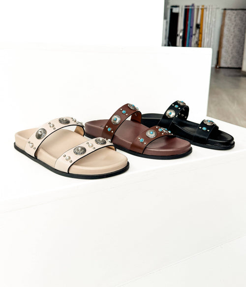 Three sandals in beige, brown, and black with decorative straps on a white background.