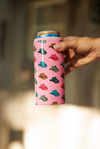 Hand holding a pink can cooler with colorful designs against a blurred background