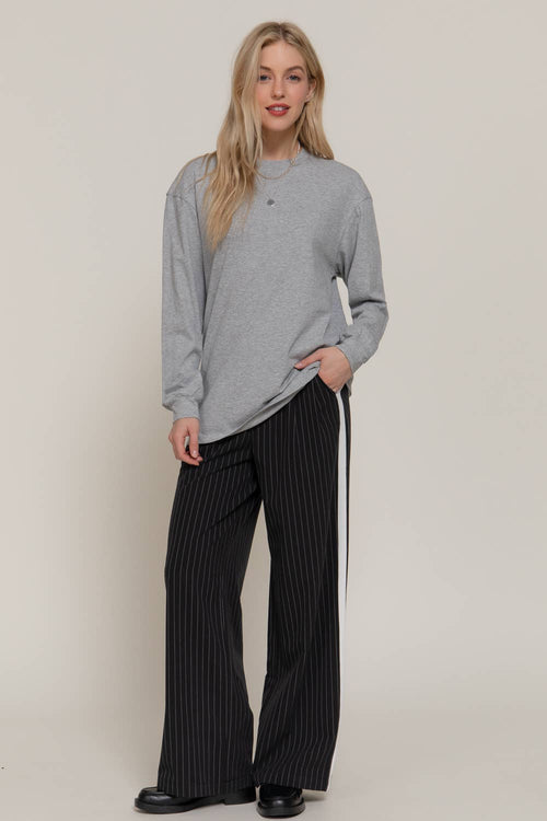 Woman wearing a gray sweater and black pinstripe pants on a plain background